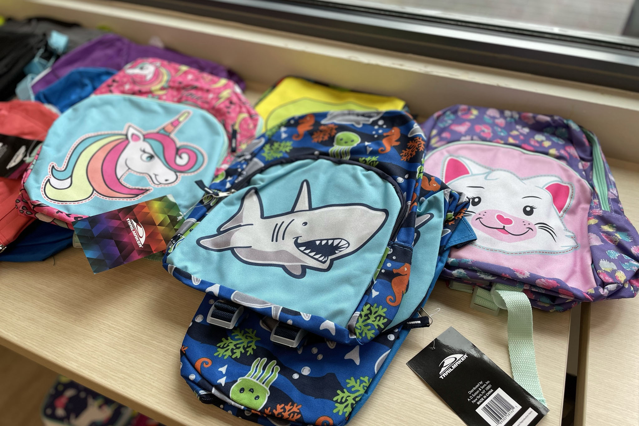 Children's backpacks laid out on a table, including ones with a cartoon shark, unicorn and cat
