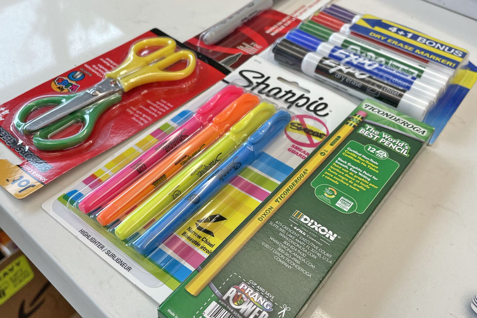 School supplies laid out on a table, including scissors, highlighters, pencils, dry erase markers and a Sharpie pen